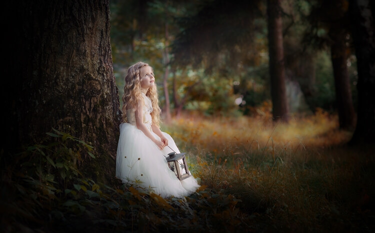 dziewczynka w białej sukience z latarenką w dłoni stoi w lesie oparta o drzewo